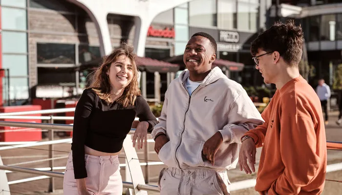3 smiling university students stood outside the University of Lincoln campus
